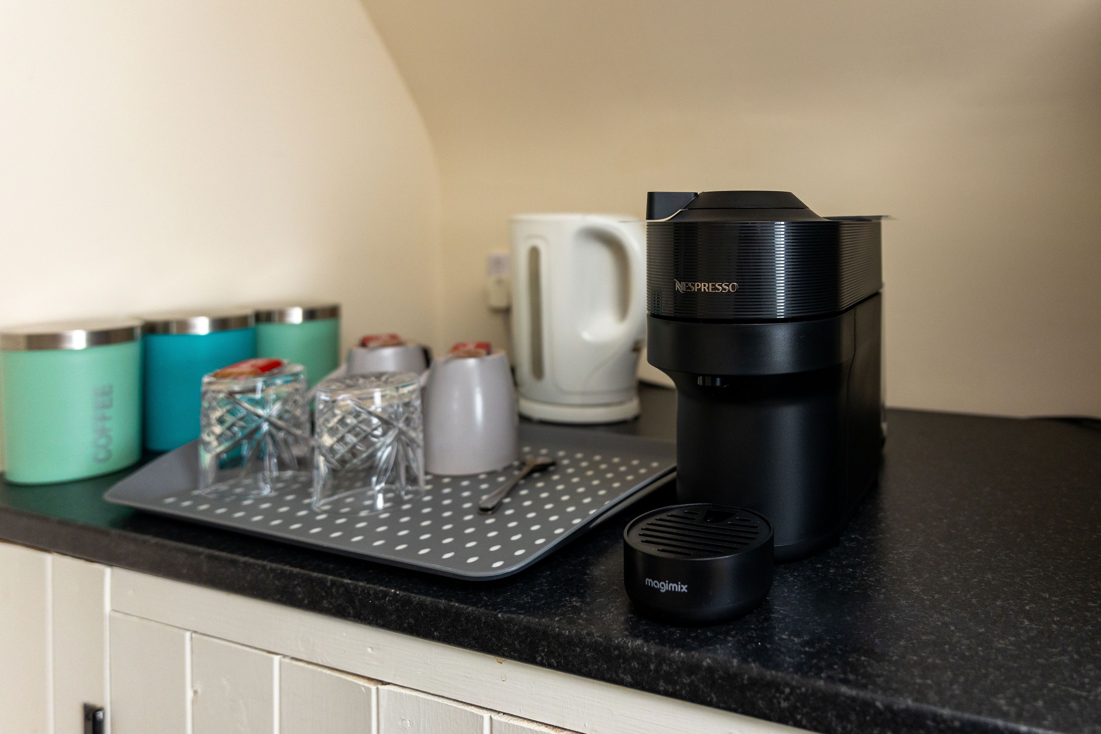 A kitchen counter with a coffee maker, a mug, and a tray with glassware.