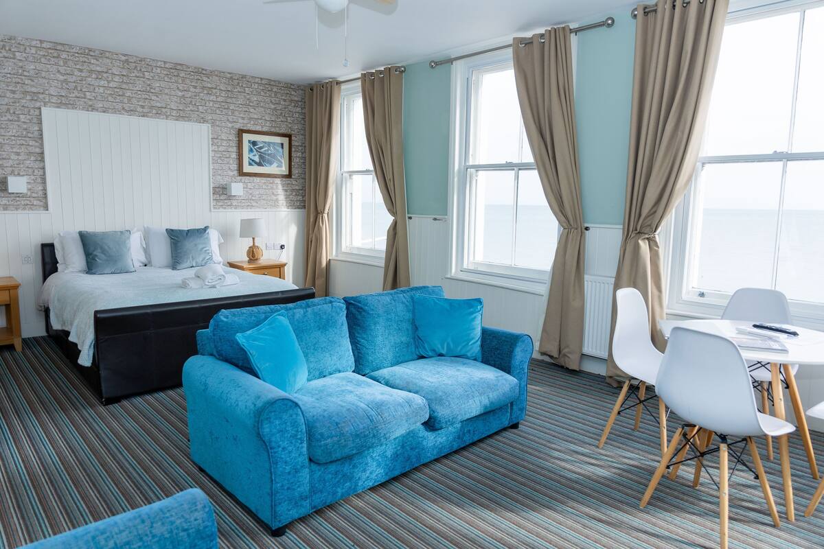 A hotel room with a bed, blue sofa, dining table, and chairs.