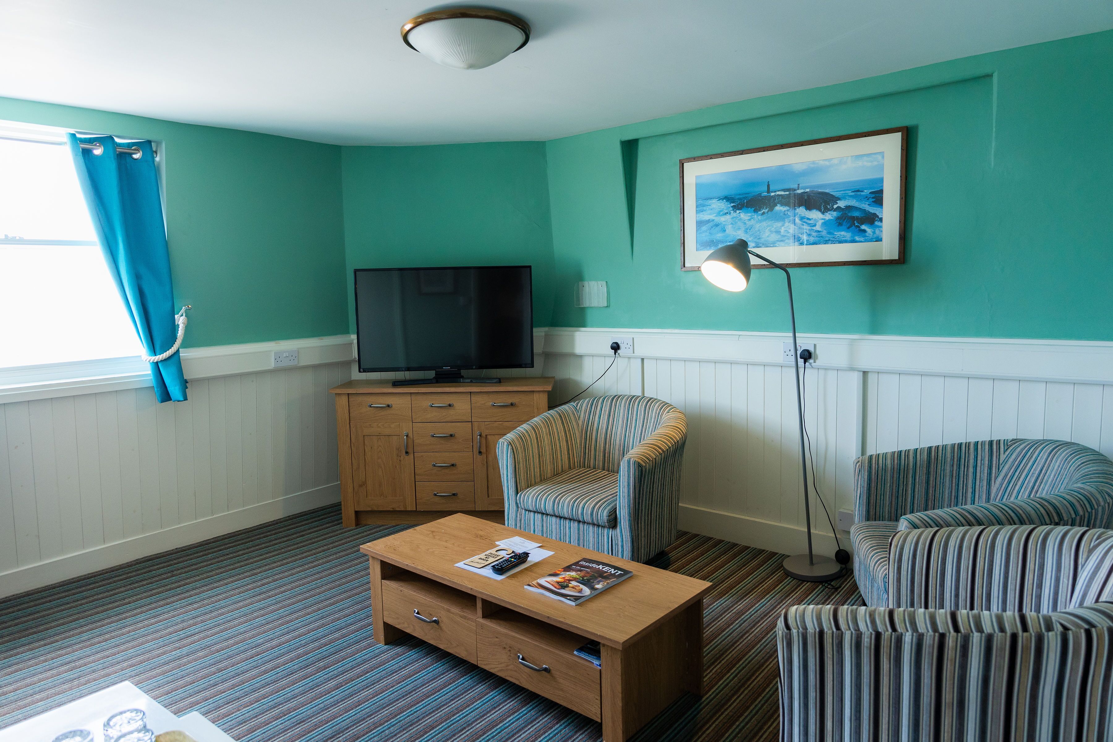 A living room with teal walls, a television, a striped armchair, a sofa, a coffee table, and a floor lamp.