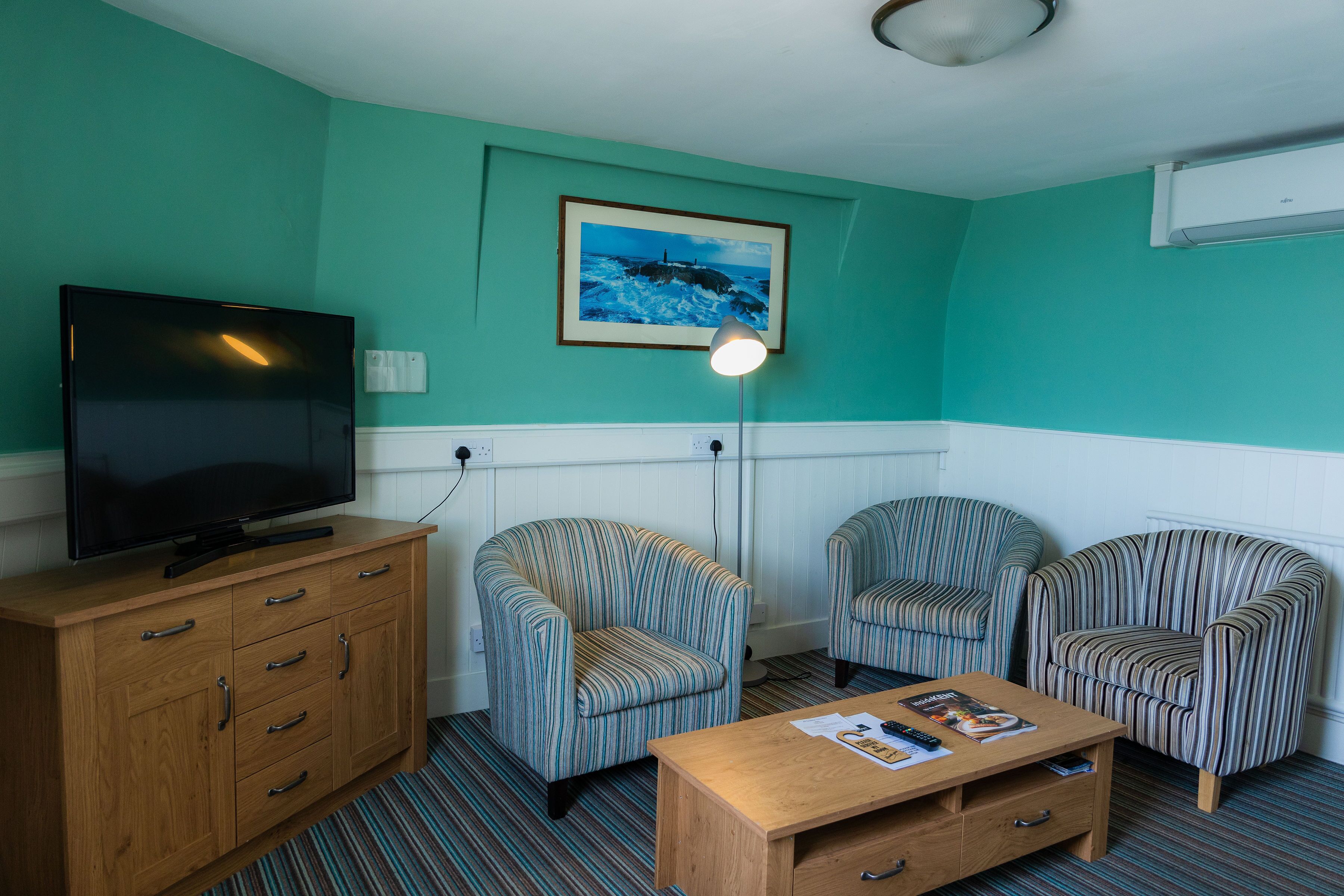 A room with teal walls, a television on a wooden cabinet, two striped armchairs, a wooden coffee table, and a framed picture on the wall.