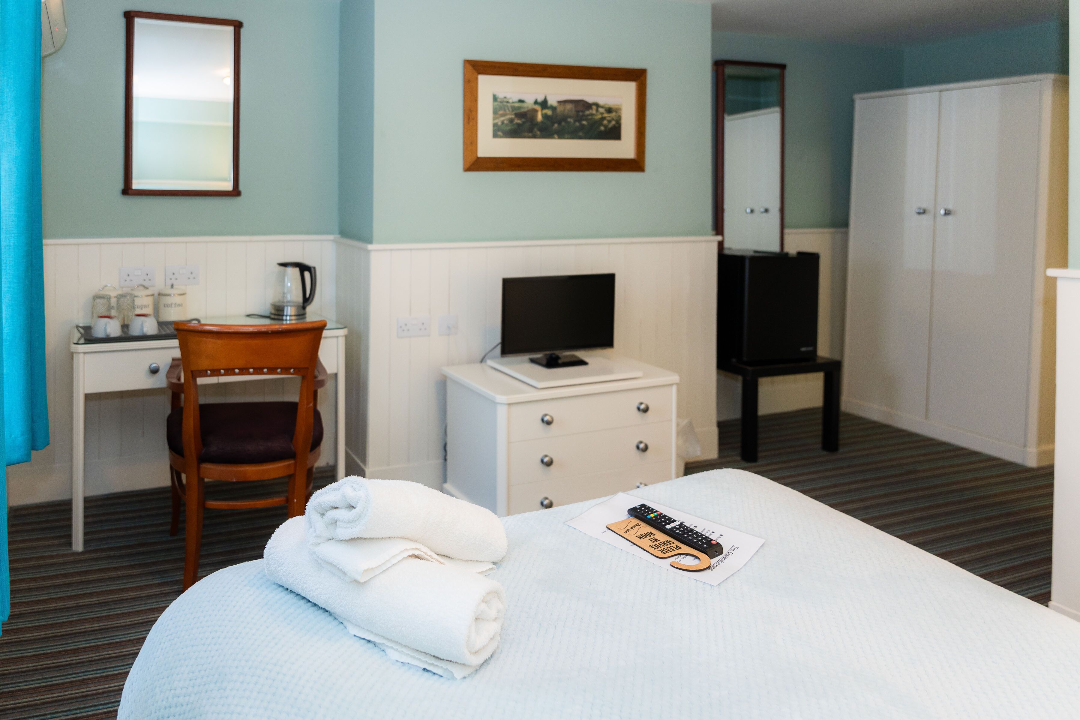 Une chambre d’hôtel comprenant un lit, un bureau avec une télévision, une chaise, une armoire et un tableau encadré au mur.