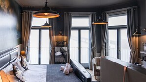 Camera d'albergo moderna con un letto grande, due lampade a sospensione, vista su un ponte e un balcone.