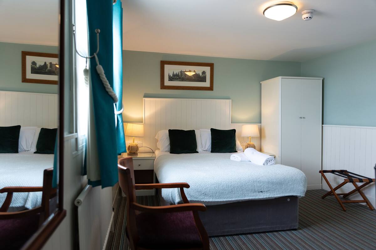 A hotel room with a bed, two chairs, a wardrobe, and a nightstand with a lamp.