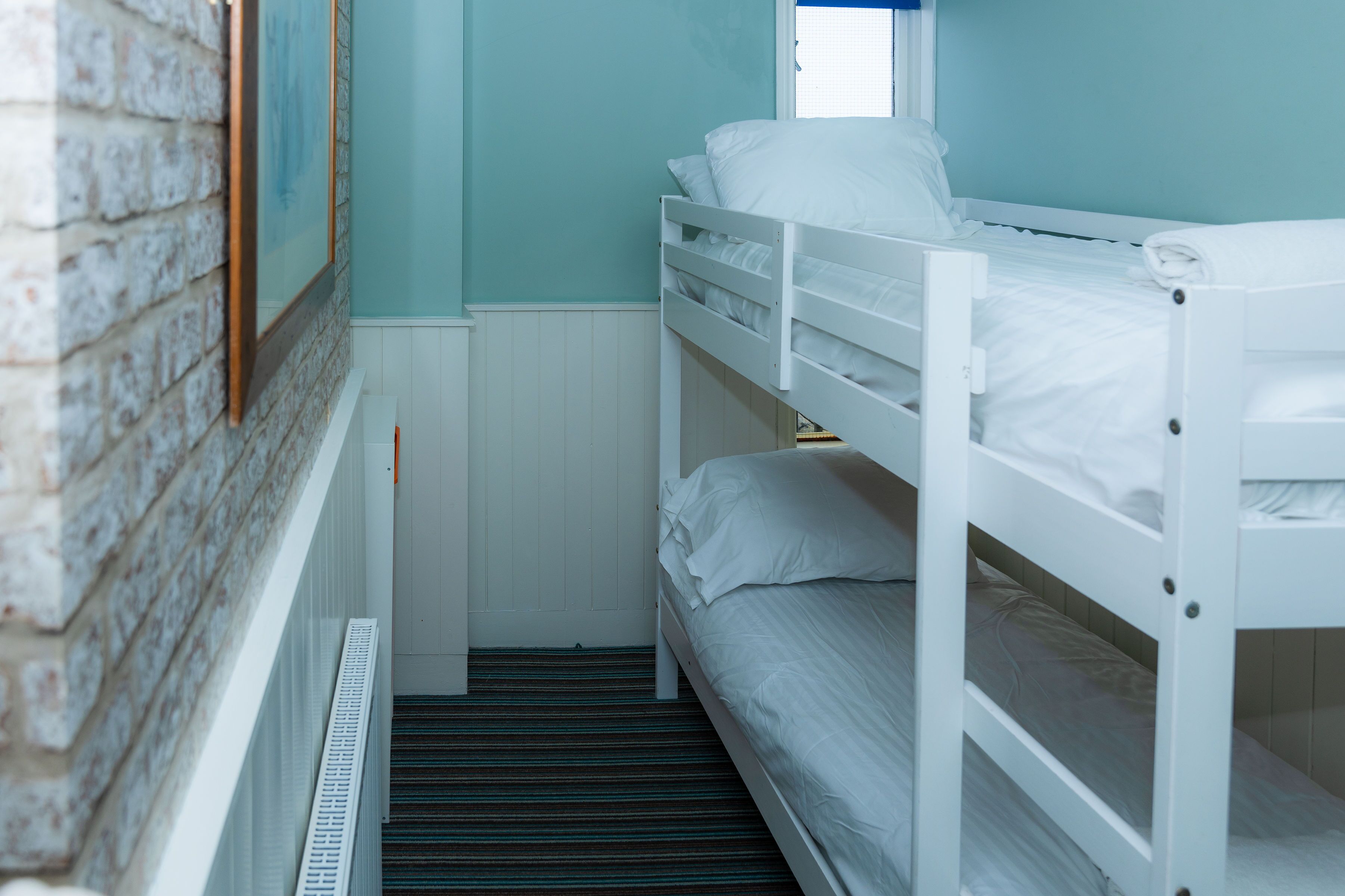 A bunk bed room with a window, white walls, and a radiator.