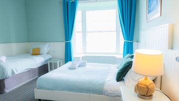 A hotel room with two beds, a window with curtains, a bedside lamp, and a framed picture on the wall.