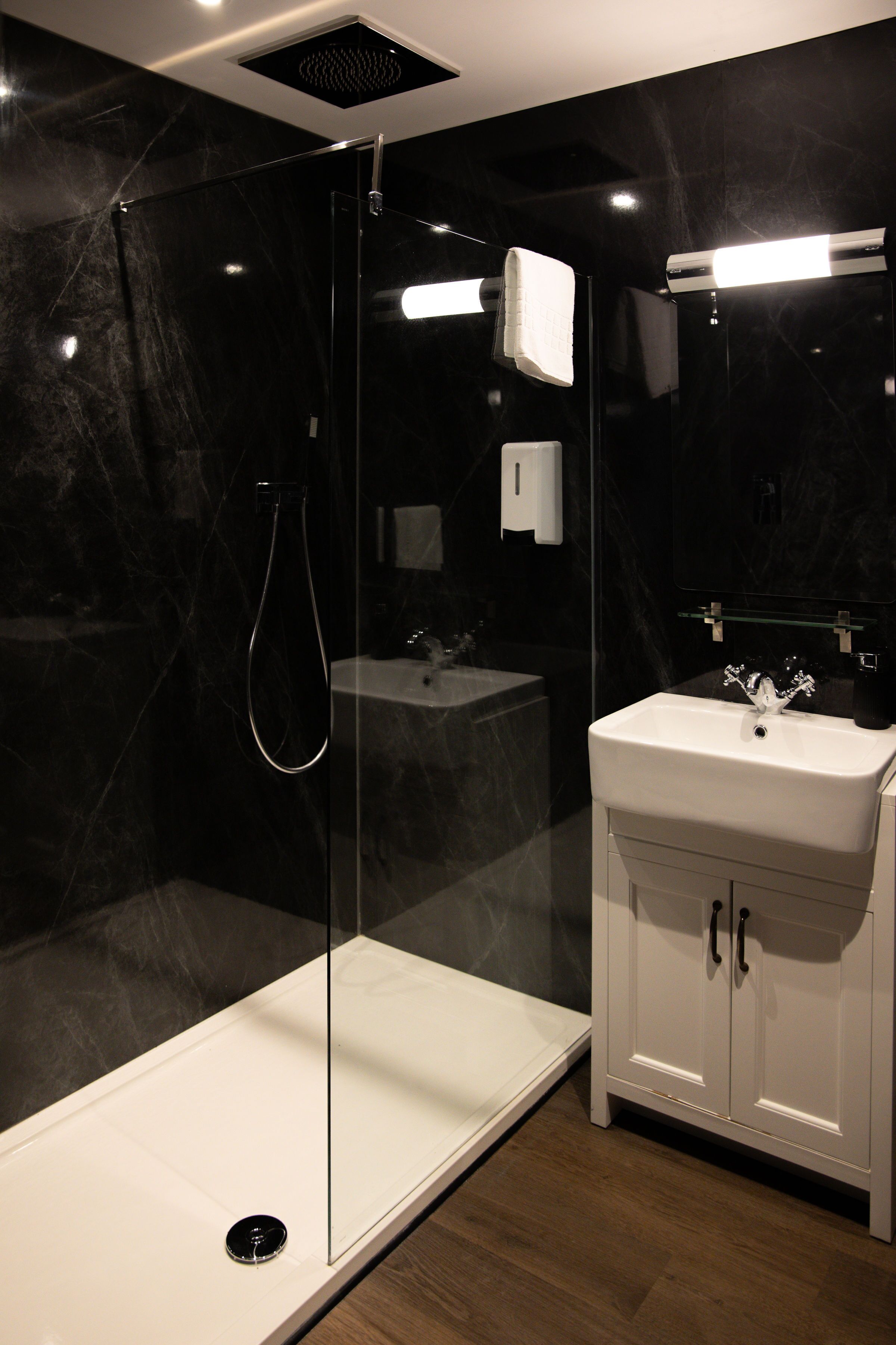 A modern bathroom with a glass-enclosed shower, a white sink, and a marble wall.