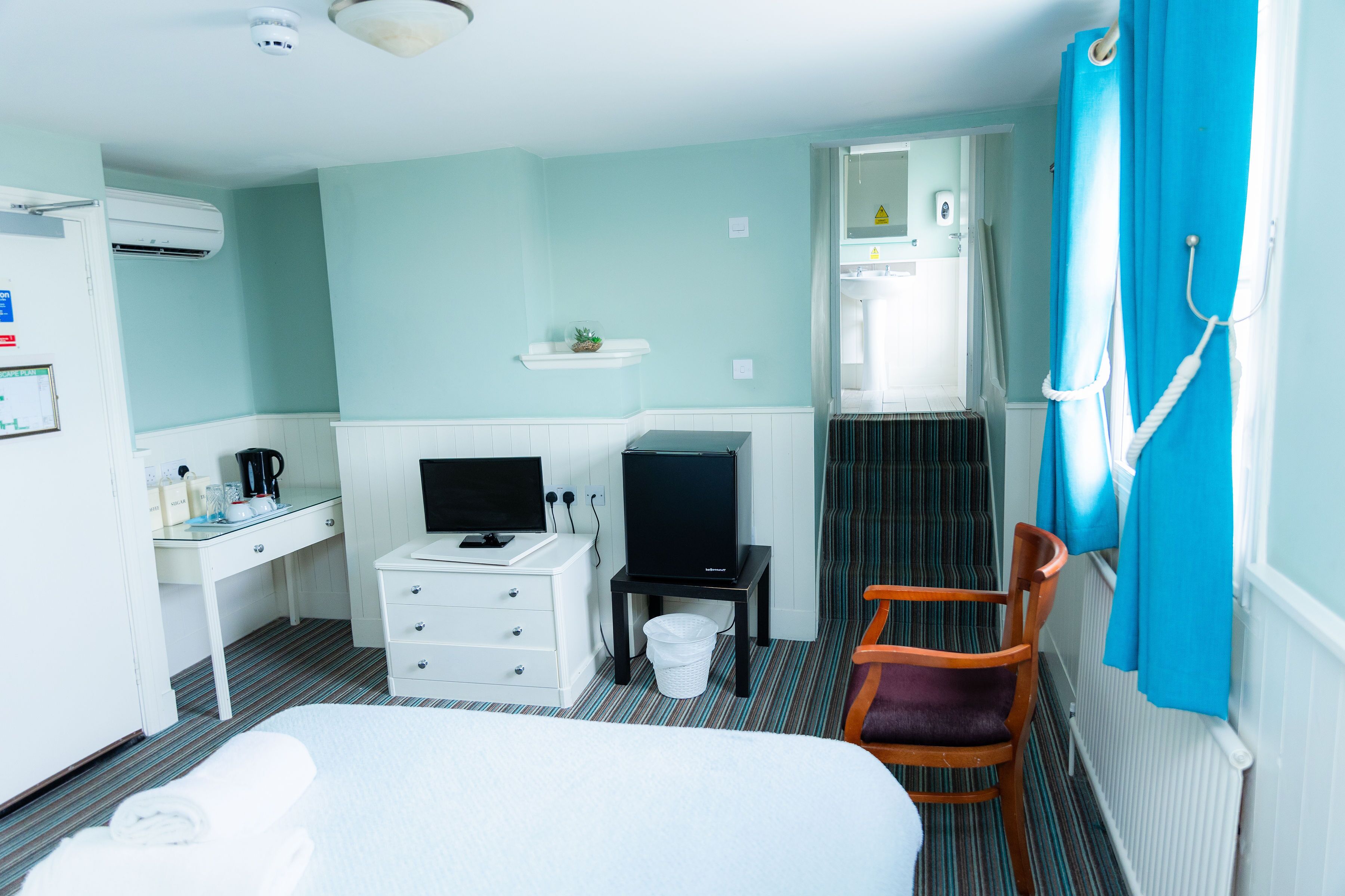 A hotel room with a bed, a desk with a computer, a television, a chair, and a bathroom with a shower curtain.