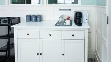 Un miniibar blanco con cafetera, teteras y una bandeja con vasos.