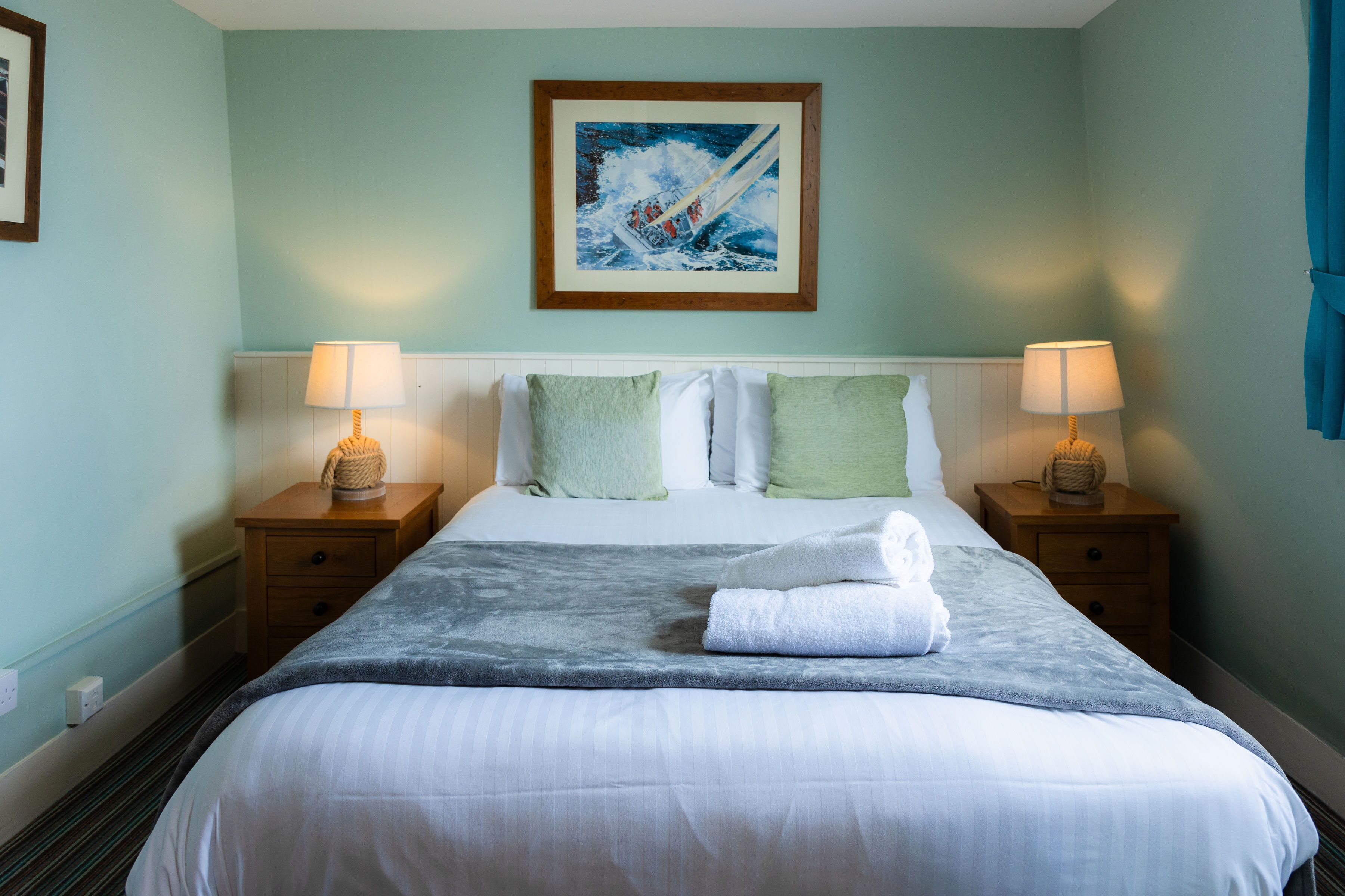 A neatly made bed with a white comforter and pillows, two bedside lamps, and a framed painting above the bed.
