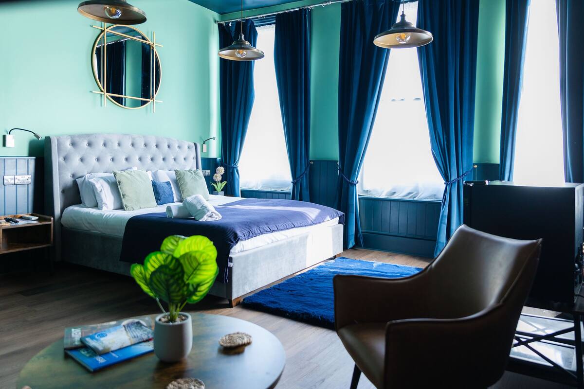 A bedroom with a large bed, a round table with a plant, and a chair.