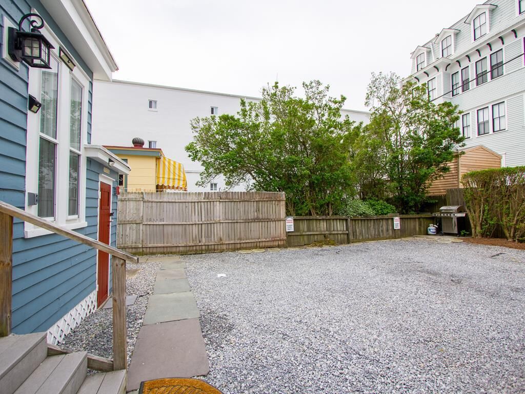 Un quartier résidentiel avec une allée en gravier, une clôture en bois et une maison avec une porte rouge.