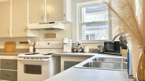 A kitchen with white cabinets, a stove, a sink, and a window with a view of a house. - Spacious 3 Bedroom 2 Bath First Floor Apt Close to Downtown Concord (Concord)