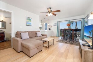 A modern living room with a sofa, a coffee table, a dining area with chairs, a ceiling fan, and a large window with a view.