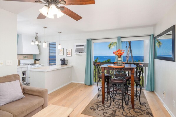 A modern kitchen with a gas stove, a dining area with a table and chairs, and a view of the ocean through large windows.