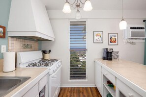 A kitchen with a gas stove, a sink, a window with blinds, and a coffee machine.