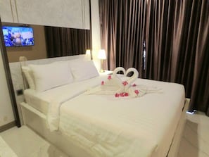 A hotel room with a neatly made bed, a flat-screen TV mounted on the wall, and a window with curtains.