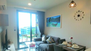 A modern living room with a sofa, a dining table, and a painting of a boat on water. - Bo202- 1 Bedroom Condo With Sea View Ao Nang Beach (Krabi)