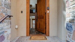 Een houten deur met een welkomstmat, stenen muren en een uitzicht op een kamer met een balkon.