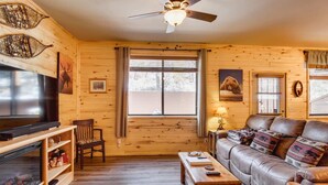 A cozy cabin interior with a wooden interior, a fireplace, a sofa, a TV, and a ceiling fan.