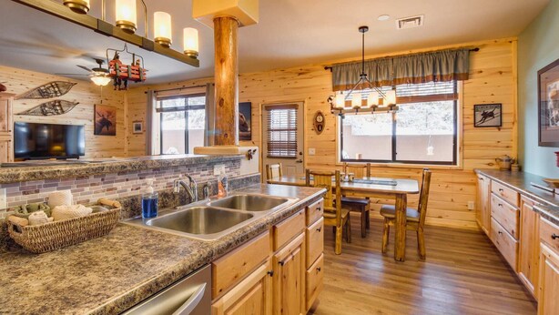 A log cabin interior with a granite countertop, stainless steel sink, wooden cabinets, and a dining area with a table and chairs.