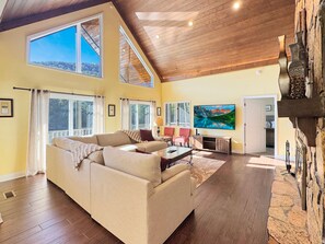A spacious living room with a large sectional sofa, a flat-screen TV mounted on the wall, and a stone fireplace.