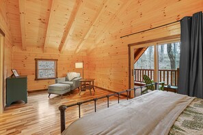 A wooden cabin interior with a bed, a small seating area, a window, and a balcony. - Green Frog | Luxury Cabin in the Woods, Hot Tub (Logan)