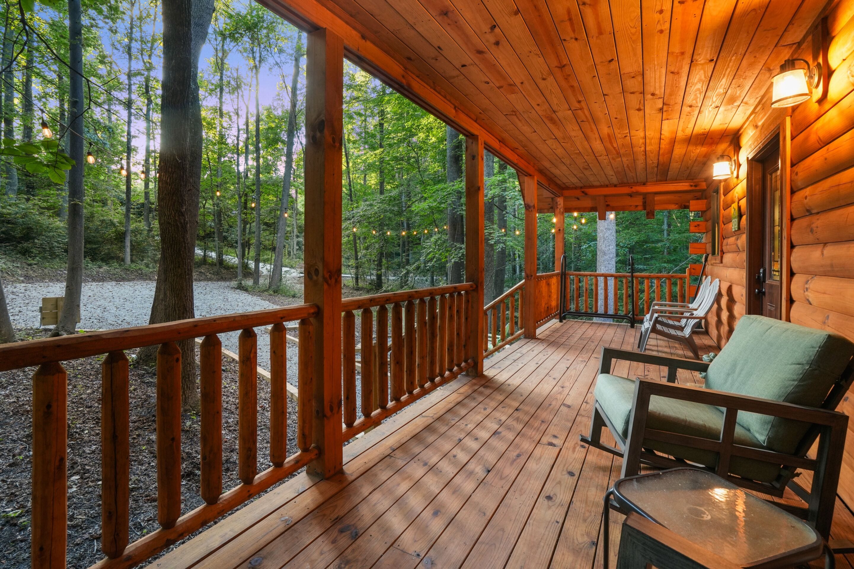 A wooden cabin with a covered porch, outdoor seating, and a view of the forest.