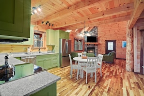 Interior de una cabaña de madera con cocina, comedor y chimenea.