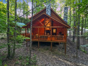 A cabin with a wooden deck and a fireplace, surrounded by trees. - Green Frog | Luxury Cabin in the Woods, Hot Tub (Logan)