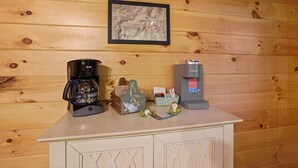 Pared de madeira com um mapa emoldurado, uma cafeteira, um bule de chá e um recipiente em formato de sapo em uma bancada.