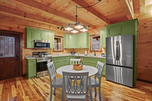 A wooden cabin interior with green cabinets, a stainless steel refrigerator, a microwave, and a dining table with chairs.