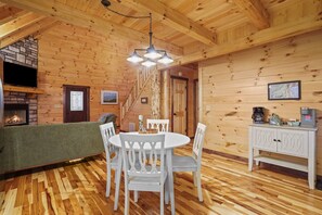 A wooden cabin interior with a dining table, chairs, a fireplace, and a staircase. - Green Frog | Luxury Cabin in the Woods, Hot Tub (Logan)
