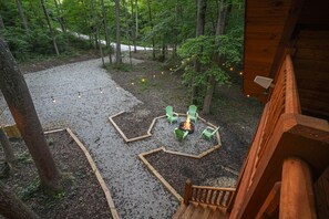 Una terraza de madera con un brasero y sillas, rodeada de árboles y grava.