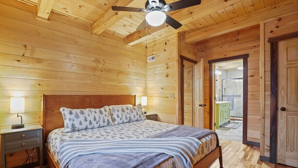 Quarto com painéis de madeira, cama, mesas de cabeceira e ventilador de teto.