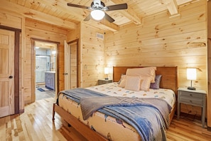 A wooden cabin bedroom with a bed, two bedside tables, and a ceiling fan. - Blue Bird | Luxury Cabin in the Woods (Logan)