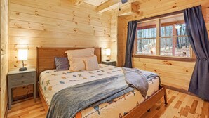 A wooden cabin bedroom with a bed, two bedside tables, a ceiling fan, and a window with curtains. - Blue Bird | Luxury Cabin in the Woods (Logan)