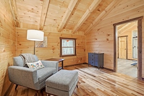 A cozy cabin interior with a sofa, ottoman, lamp, and a small table. - Blue Bird | Luxury Cabin in the Woods (Logan)