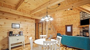 A wooden interior with a dining area, white furniture, a fireplace, and a stone wall. - Blue Bird | Luxury Cabin in the Woods (Logan)