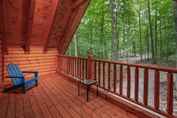 A wooden deck with a blue Adirondack chair and a small table, overlooking a forested area.