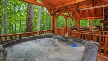 A wooden deck with a hot tub surrounded by a forest.