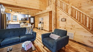 A cozy cabin interior with a wooden staircase, a kitchen area, and a living room furnished with a sofa and armchairs. - Blue Bird | Luxury Cabin in the Woods (Logan)