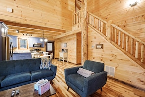A wooden interior with a kitchen, a staircase, a sofa, and a coffee table. - Blue Bird | Luxury Cabin in the Woods (Logan)