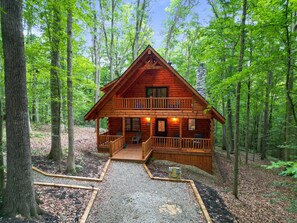 A log cabin with a balcony, a porch, and a gravel driveway. - Blue Bird | Luxury Cabin in the Woods (Logan)