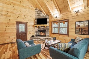 A cozy cabin interior with a stone fireplace, wooden walls, and a television mounted above it. - Blue Bird | Luxury Cabin in the Woods (Logan)