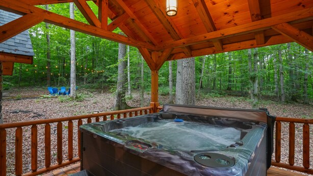 A hot tub on a wooden deck with a view of a forest. - Blue Bird | Luxury Cabin in the Woods (Logan)