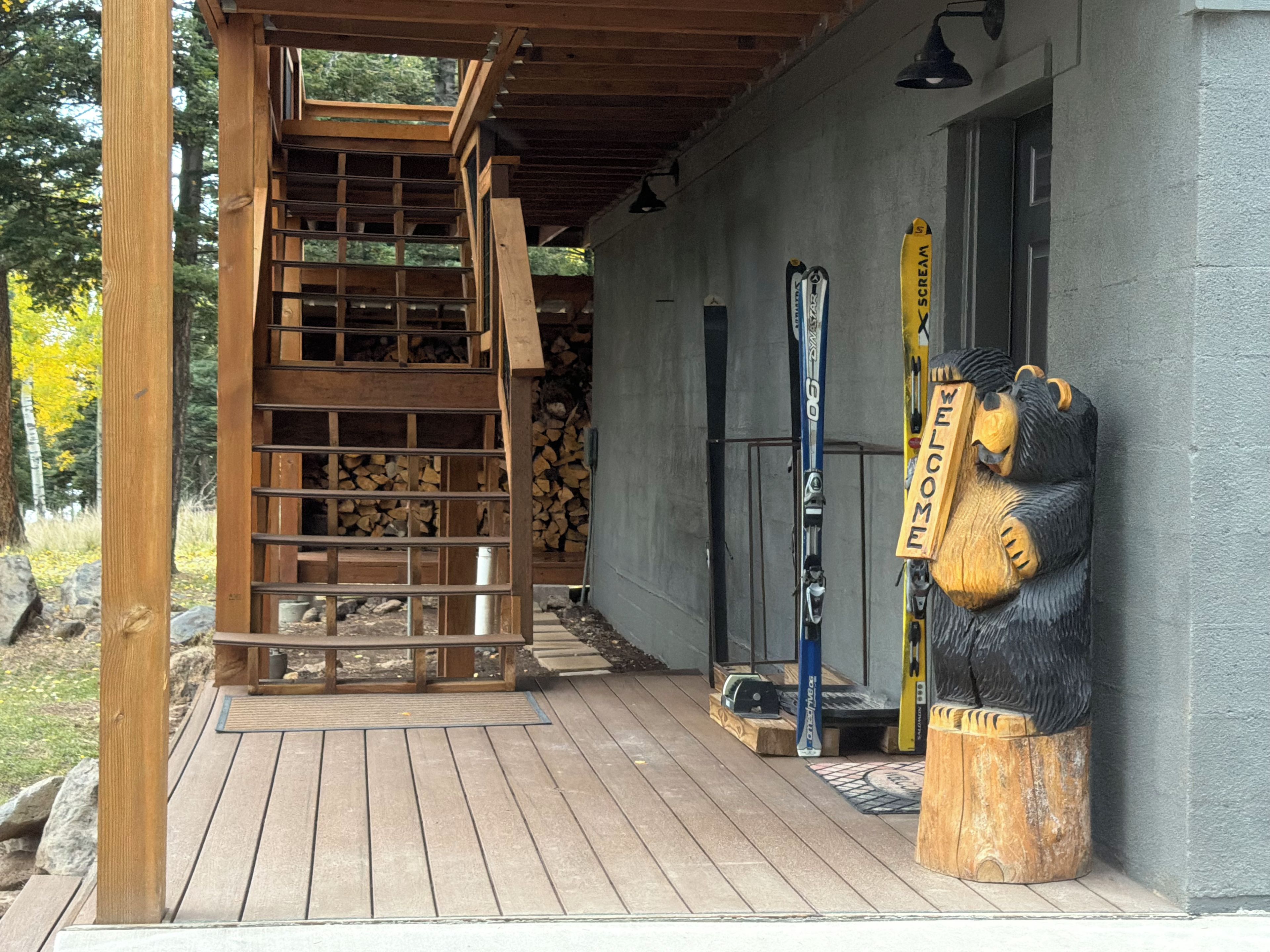 Un escalier en bois mène à un espace abrité où se trouvent un banc et une sculpture d’ours en bois.