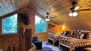 Eine Holzhütte mit Schlafzimmer im Obergeschoss, Deckenventilator, großem Fenster und rustikaler Einrichtung.