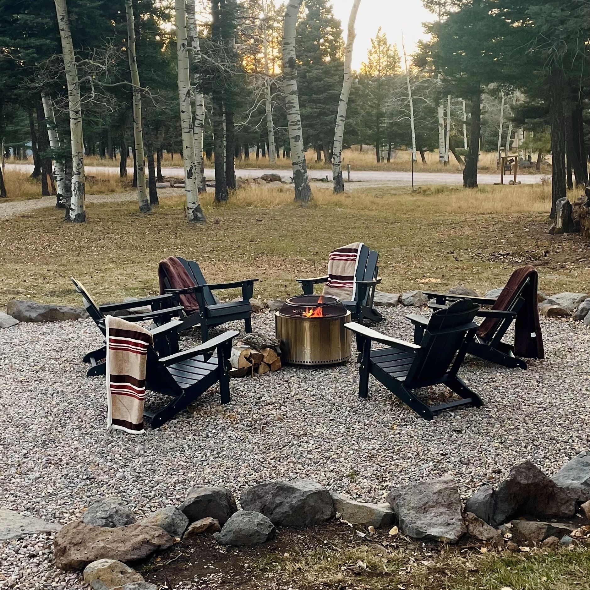 An outdoor seating area with Adirondack chairs and a fire pit surrounded by gravel and rocks.