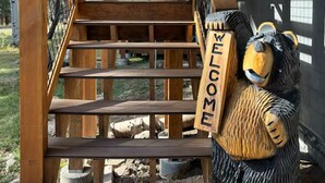 Eine Holztreppe führt zu einer Terrasse, auf der eine Bärenskulptur ein Schild mit der Aufschrift "WILLKOMMEN" hält.