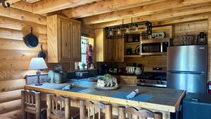 Eine holzgetäfelte Kücheneinrichtung im Landhausstil mit einer zentralen Kochinsel, Holzstühlen, einem Herd und einem Kühlschrank.